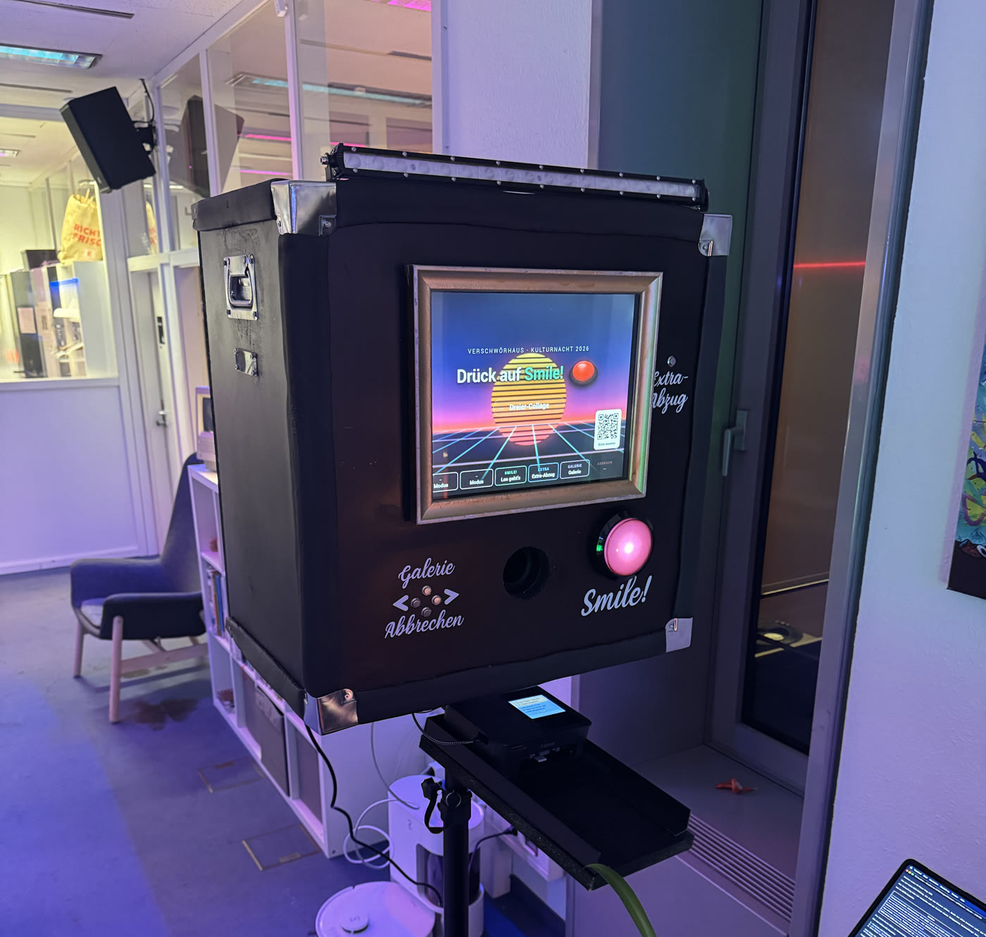 The photo booth close up: a black flight case with a gilded picture frame around the touchscreen, a glowing pink shutter button and labels for gallery and extra print